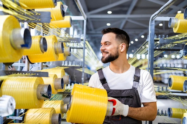 Worker changing thread spool on industrial knitting machine inside textile factory