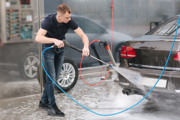 Worker cleaning car using high pressure water.