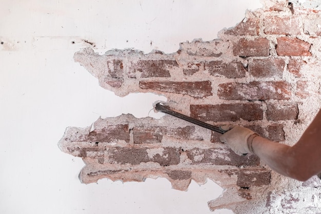 労働者が古いレンガの壁を剥がす石膏で掃除する古い家の改修