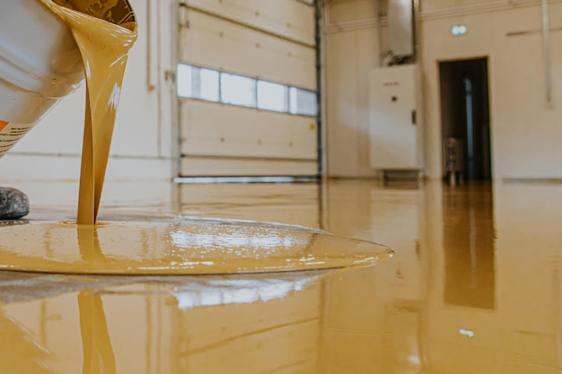 Photo worker coating floor with selfleveling epoxy resin in industrial workshop