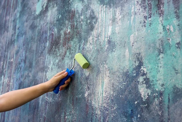 Рабочий в комбинезоне рисует стену с роликом в зеленом цвете крупным планом