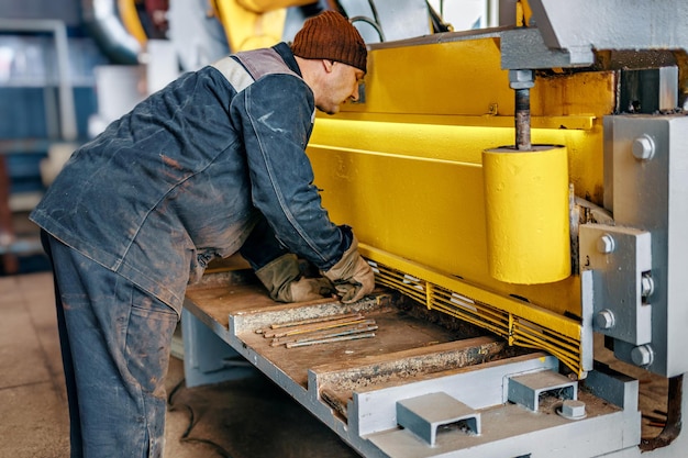 Il lavoratore taglia il metallo su una macchina meccanica a ghigliottina nella sala di produzione attrezzature industriali per il taglio di metalli scena reale