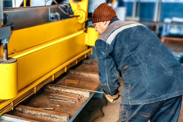 Worker cuts metal on mechanical guillotine machine in\
production hall industrial equipment for metal cuttingreal\
scene