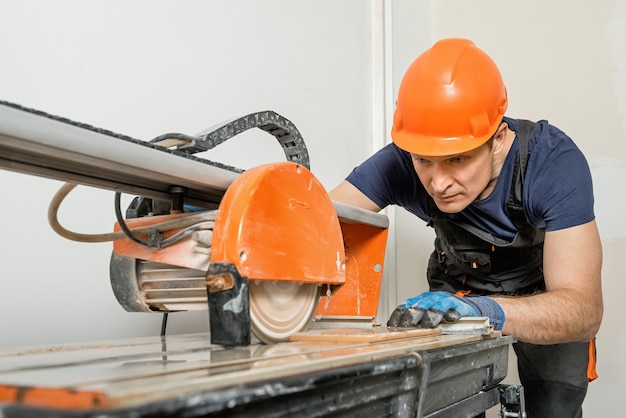 The worker cutting a ceramic tile on a wet cutter saw machine