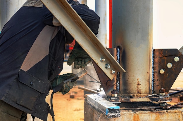 Lavoratore che taglia la lamiera con la torcia a gas in un cantiere installazione di una struttura metallica primo piano il saldatore esegue l'installazione di strutture metalliche scintille dalla saldatura