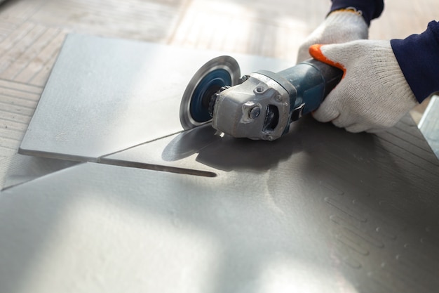 Photo worker cutting a tile using an angle grinder at construction site