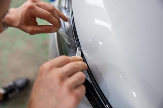 Worker detailer cutting off excess of polymer protective outer coating. Closeup on hand of car service master