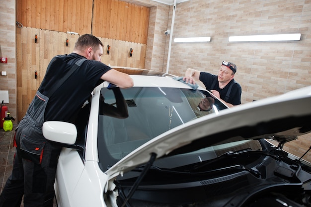 Worker in detailing garage put polyurethane anti-gravel film cover in white luxury car.