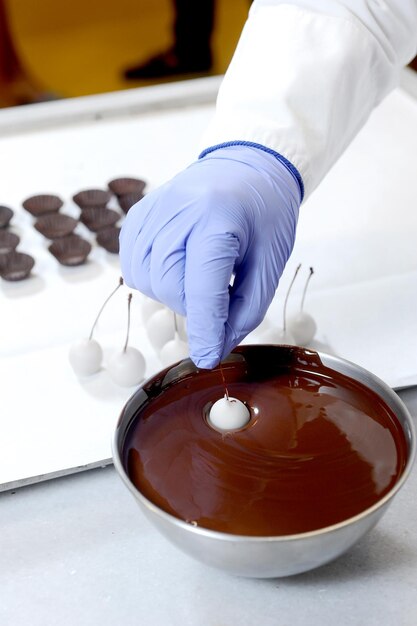 Photo worker dipping cherries into bowl of chocolate at the chocolate factory