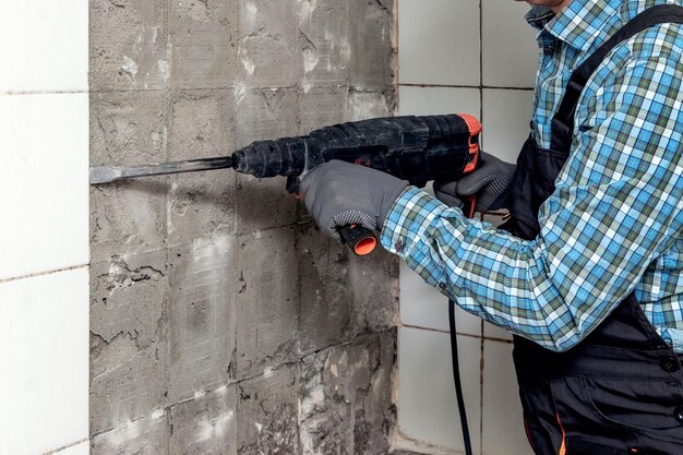 A worker dismantles facing tiles in the bathroom using a perforator