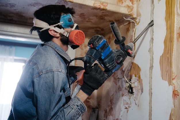 労働者は、穴あけ器を使用して壁を掘削します。アパートの修理