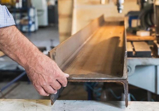 A worker in a factory holds two metal beams before drilling holes in them