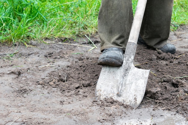 Worker farmer man legs digging soil, ground with shovel in rubber boots in garden, close up