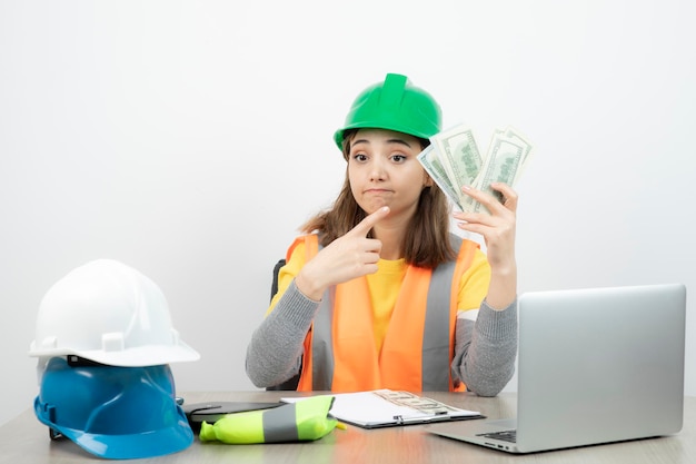 Worker female in orange vest and green helmet sitting at the desk . High quality photo