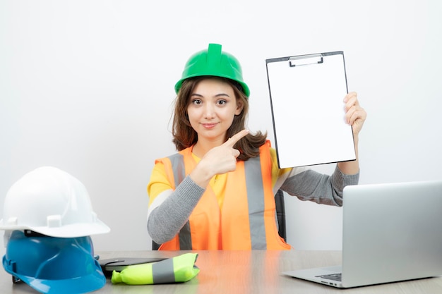 Operaia in uniforme seduta alla scrivania con laptop e appunti. foto di alta qualità