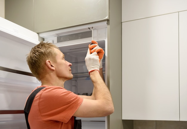 Worker fixing the built in refrigerator in the kitchen furniture