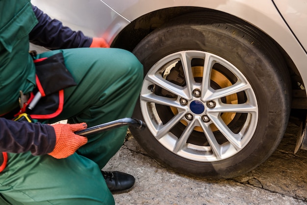 Worker fixing car wheel with spanner close up