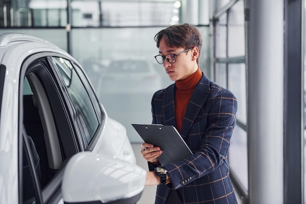 Worker in formal wear with notepad looking at modern car.