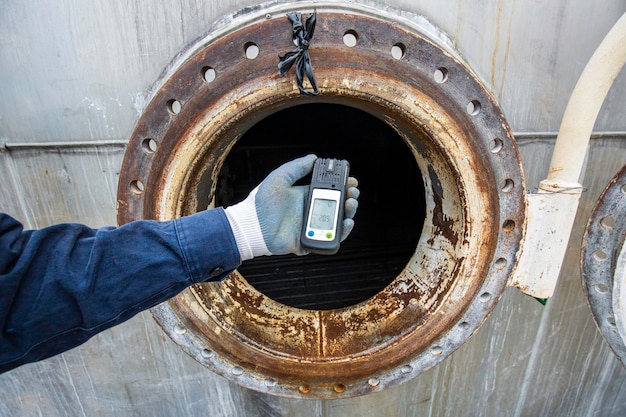 Рабочий держит газовый детектор, проверяя безопасность, тестируя газ на переднем люке из нержавеющей стали