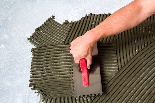 床にモルタル接着剤を作るタイルのインストールのためのこてツールと労働者の手