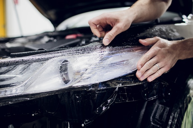 Worker hands installs car paint protection film wrap auto headlight