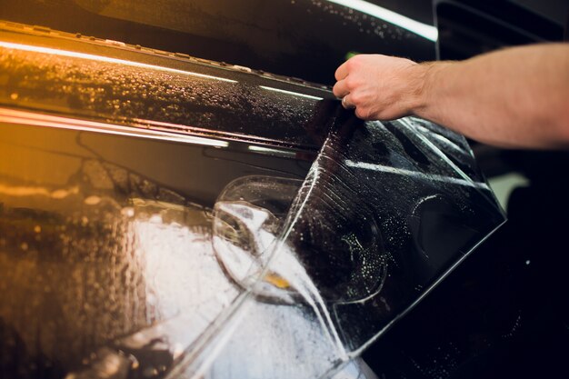 Worker hands installs car paint protection film wrap.