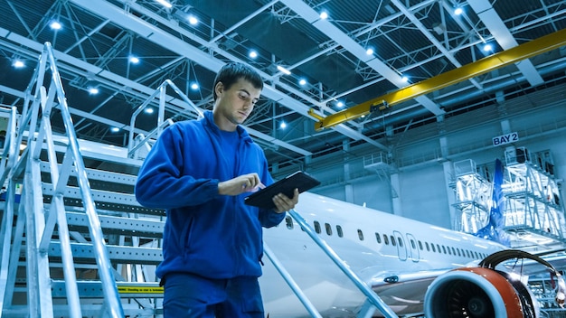 Foto un lavoratore in un hangar controlla su un tablet.