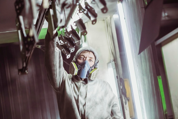 Worker hangs up parts before painting in a factory