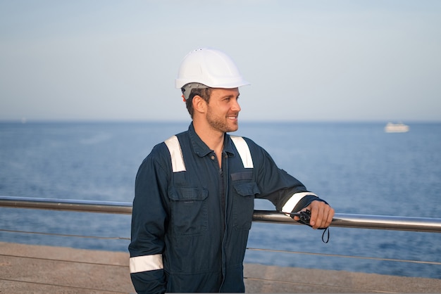 Worker in helmet standing near sea