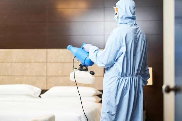 Worker holding the disinfectant and pointing it towards the middle of the room