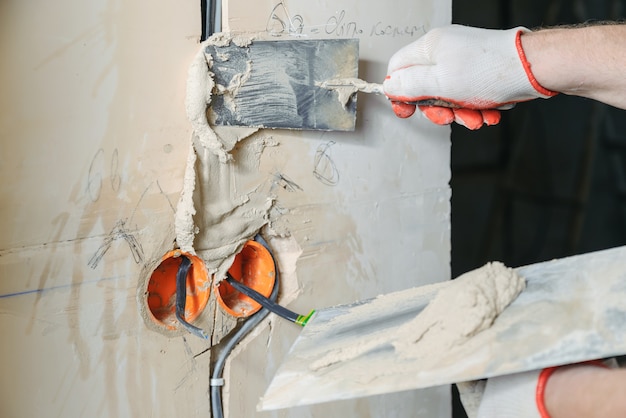 Worker holding trowels with gypsum