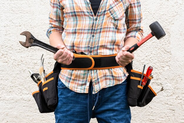 A worker holds an adjustable wrench and a hammer