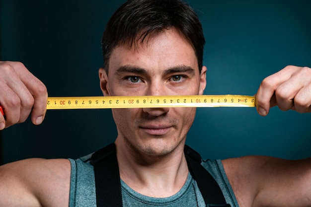 worker holds a tape measure in front of his face.