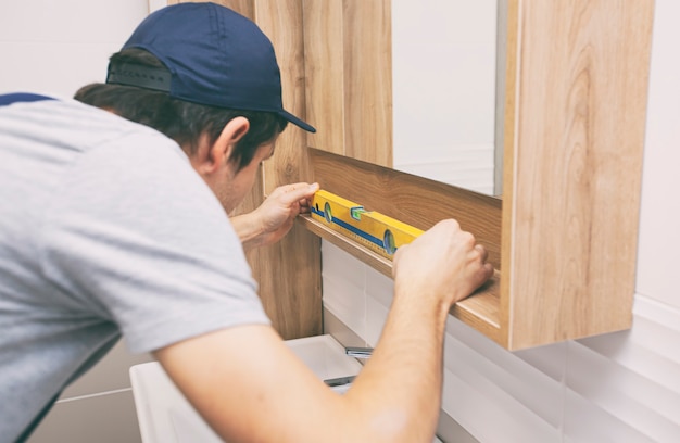 The worker installs the mirror in the bathroom