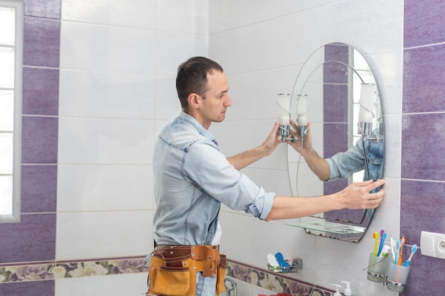 The worker installs the mirror in the bathroom