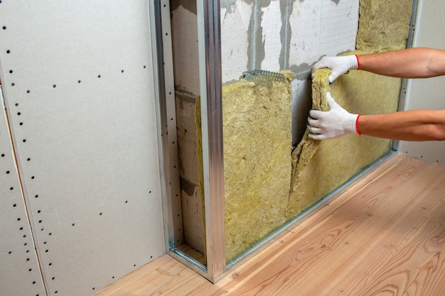 Worker insulating a room wall with mineral rock wool thermal insulation.