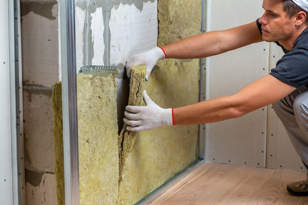 Worker insulating a room wall with mineral rock wool thermal insulation.