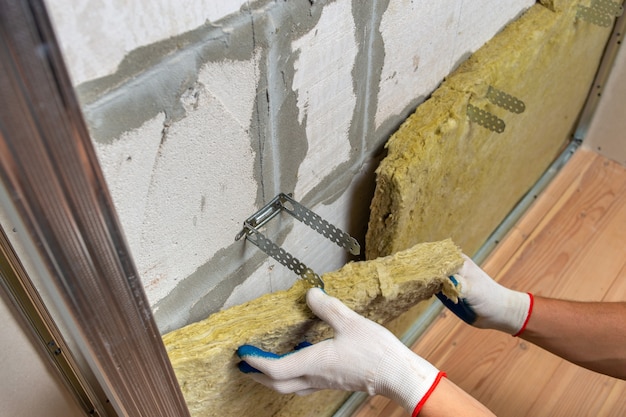 Worker insulating a room wall with mineral rock wool thermal insulation.