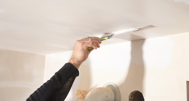 Photo worker is applying putty on a ceiling renovating house