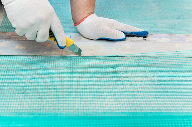 A worker is cutting off a piece of fiberglass mesh with a knife