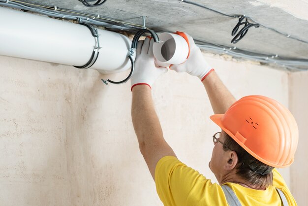 The worker is installing a ventilation system in the apartment