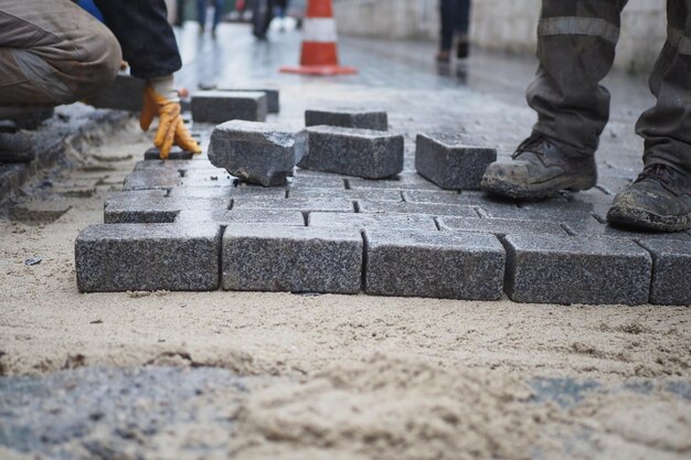 Рабочий кладет бетонные кирпичи друг на друга для строительства нового тротуара