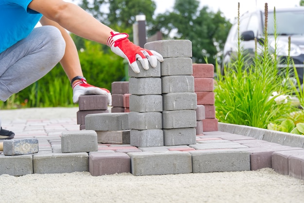 worker laying paving stones. stone pavement, construction worker laying cobblestone rocks on sand.