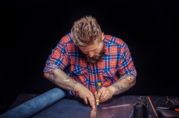 Worker of leather demonstrates leather cutting process.