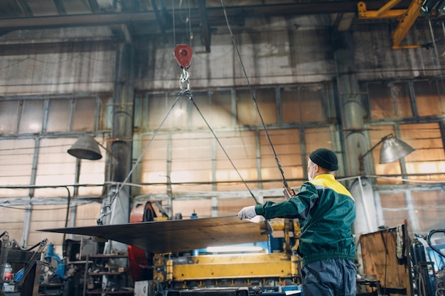 사진 산업 공장 공장에서 원격 컨트롤러와 후크가 있는 크레인 체인 호이스트가 있는 작업자 리프트 금속 시트