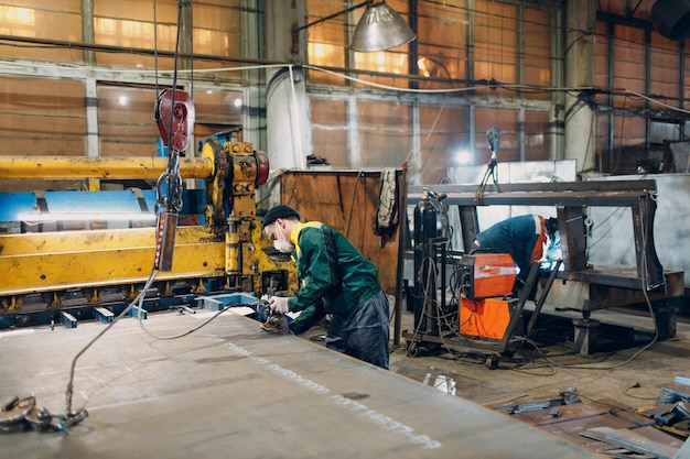 作業員は、リモートコントローラーと産業工場の工場でフック付きのクレーンチェーンホイストで金属板を持ち上げます