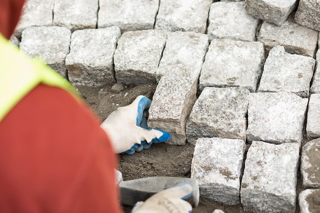 Worker made sidewalk from bricks using hammer in hand, over the shoulder view. maintenance work on paving with interlocking paving stones