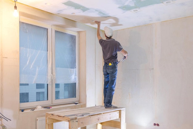 労働者は、新しいアパートの男漆喰の壁と天井で修理を行います