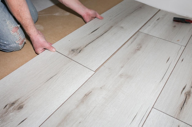 Worker making laminate flooring in apartment Maintenance repair renovation Wooden parquet planks indoors