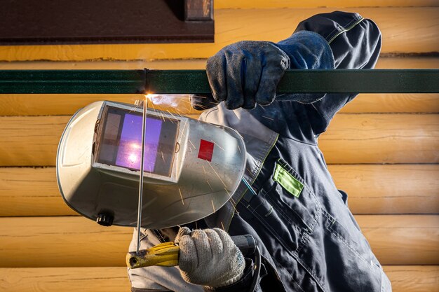 Рабочий мужчина-сварщик на строительной площадке сваривает металлическую конструкцию на заборе, процесс сварки